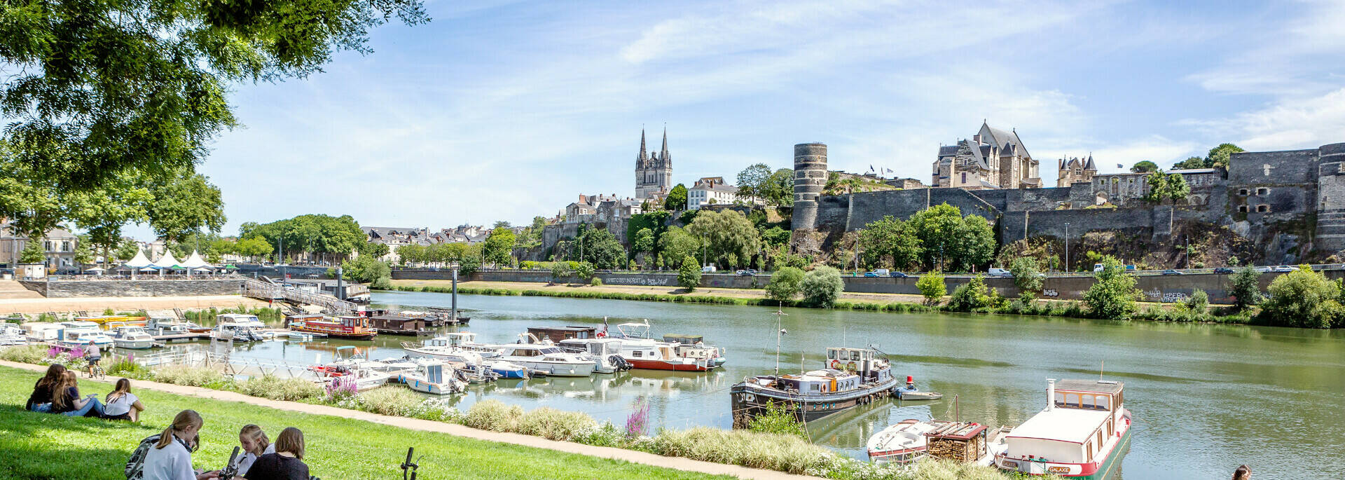 Young people sitting on the grass near the port of Savatte, facing the Maine and the castle of Angers.