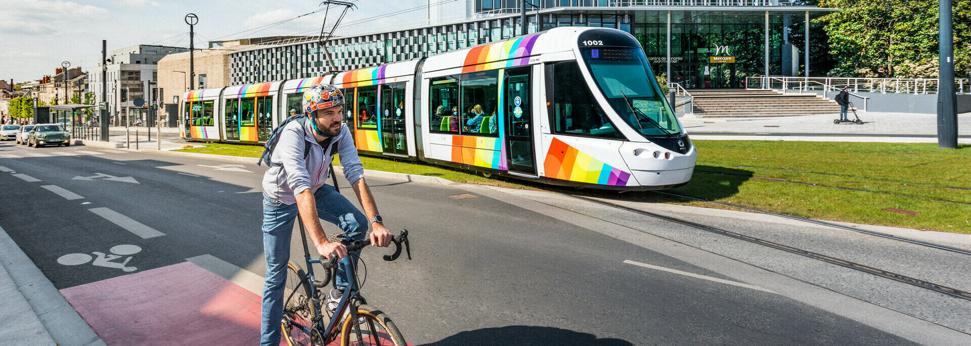 Homme à vélo avec le tram passant derrière, devant le Centre de Congrès d'Angers