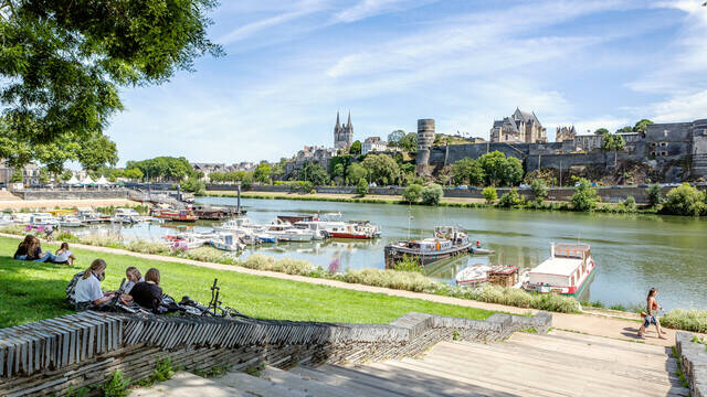 Young people sitting on the grass near the port of Savatte, facing the Maine and the castle of Angers.