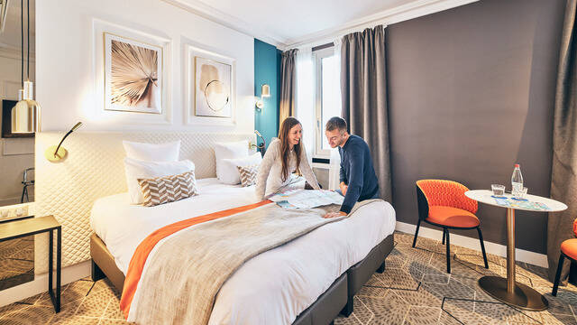 Pareja hablando frente a un plano sentada en la cama de una habitación de hotel