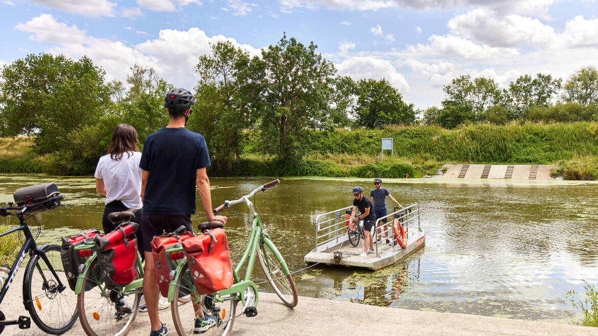 2 cyclistes qui attendent le retour du bac où se tiennent deux personnes à bord