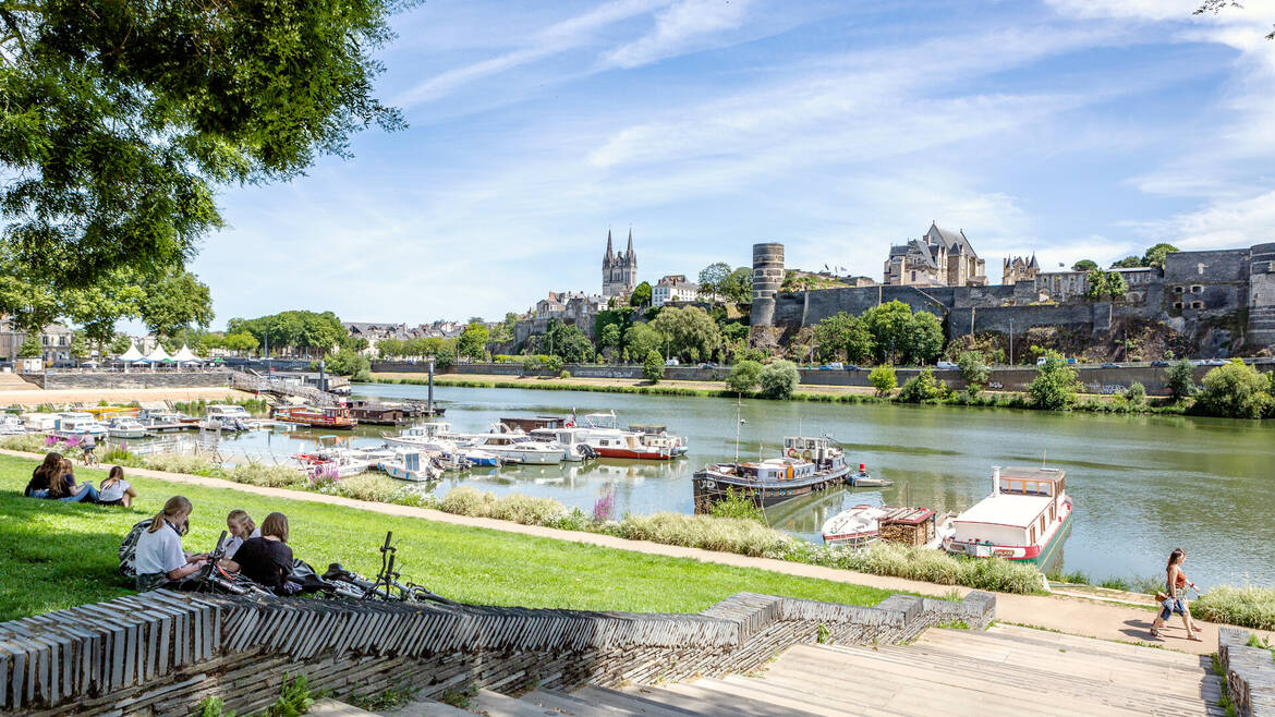 Jóvenes sentados en la hierba cerca del puerto de Savatte, frente al río Maine y el castillo de Angers.