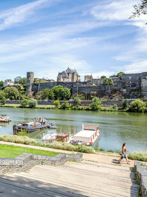 Jeunes gens assis sur l'herbe près du port de la Savatte, face à la Maine et au château d'Angers.